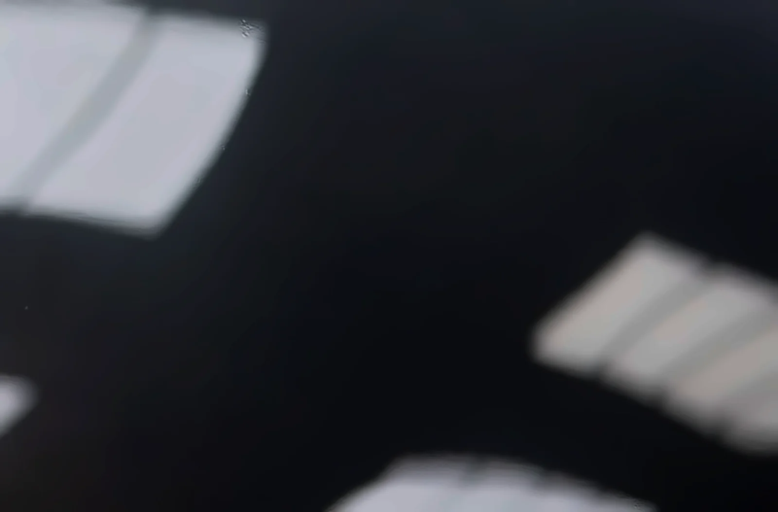 A gloss black car panel split in two, one half protected with paint protection film and one half bare, both with light swirl marks