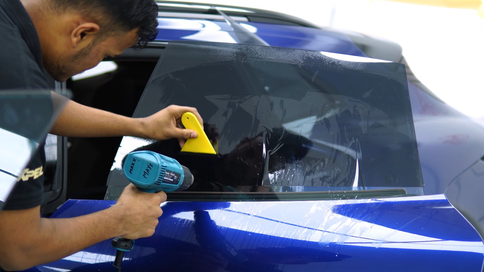 Window film being heat-shaped on the rear glass of a blue Porsche Taycan